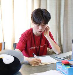 Boy in SUMaC writing out a math problem in marker next to a laptop