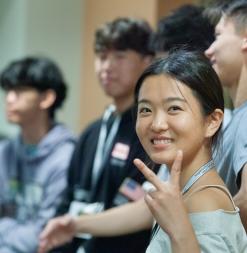 A participant turns and smiles while making a peace sign with her hand